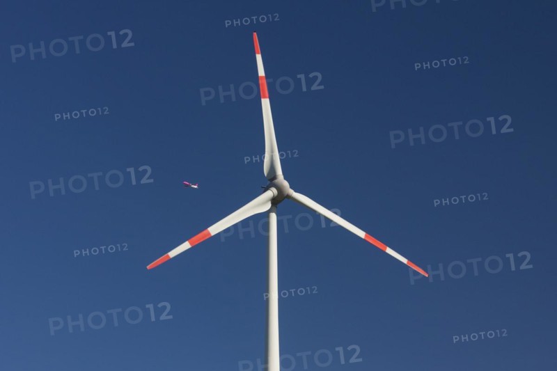 Jet airliner seen through blades of wind turbine against blue sky