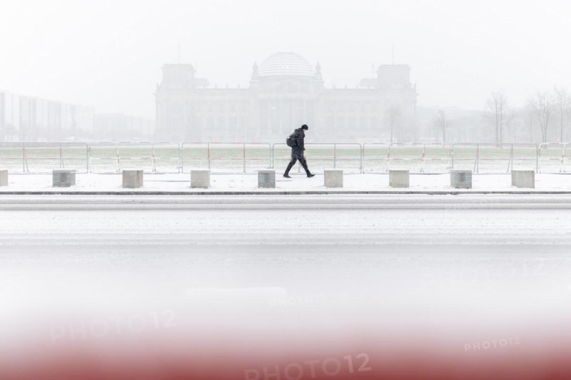 A person stands in front of the Bundestag in the driving snow in Berlin