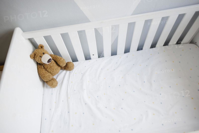 Symbolic photo on the subject of wanting a child. A teddy bear sits in an empty cot. Berlin