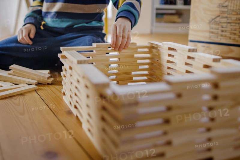 Symbolic photo on the subject of creative play among children. A boy builds with wooden building blocks. Berlin