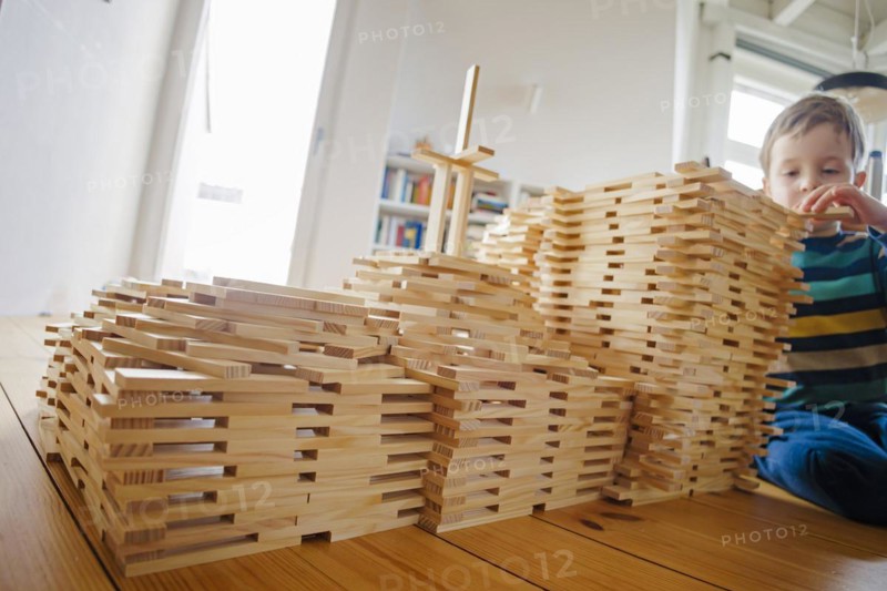 Symbolic photo on the subject of creative play among children. A boy builds with wooden building blocks. Berlin