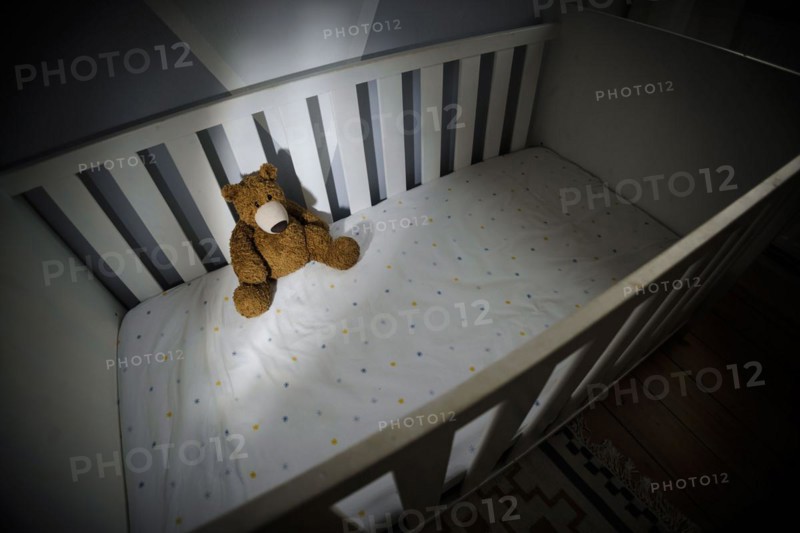 Symbolic photo on the subject of child abuse. A teddy bear sits in an empty cot. Berlin