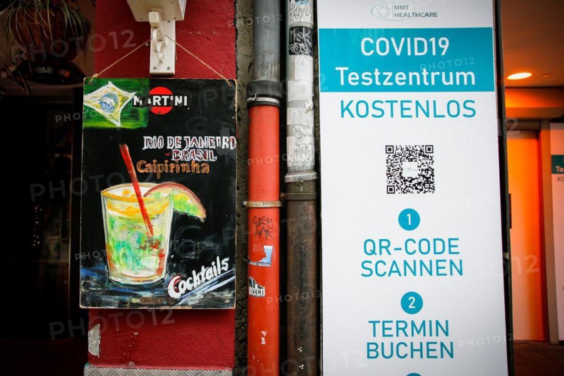 A board of a bar advertising Caipirinha cocktails stands next to the sign of a Covid-19 test centre in the old town of Duesseldorf