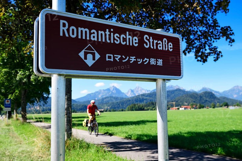 Cyclist in front of sign Romantic Road with translation in Japanese
