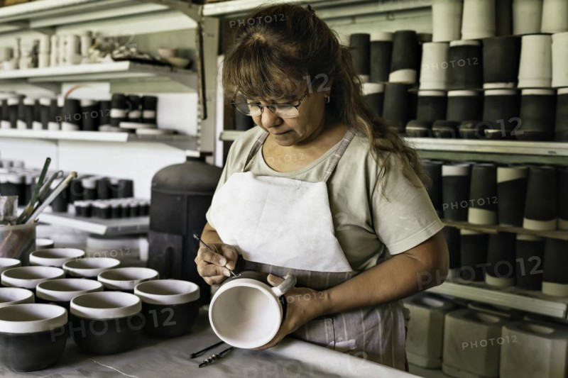 Middle-aged woman craftswoman with apron making the sgraffito on a piece of pottery