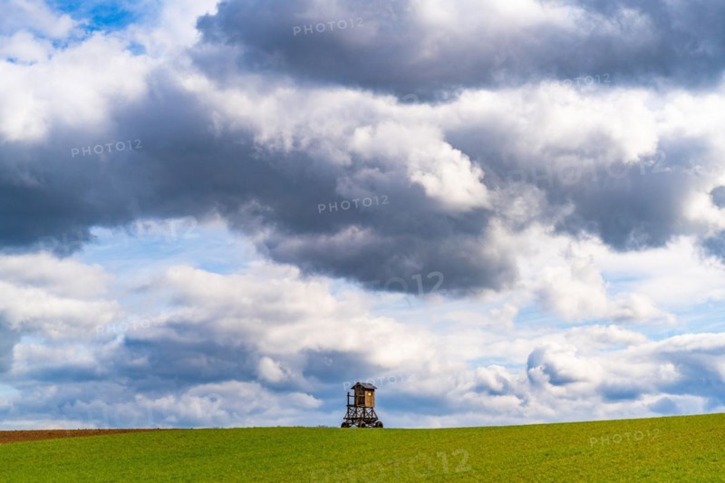 Mobile raised hide in an empty field under dramatic clouds