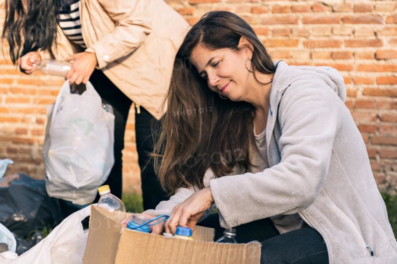 Women helping in organizing recyclable material. In the foreground a happy woman saving plastic bottles in a cardboard box