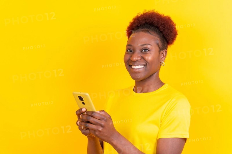 Young african american woman isolated on a yellow background smiling with the mobile phone