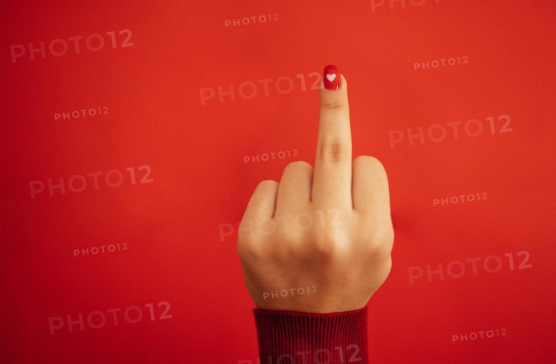 Fuck you hand sign. Female hand with bright red manicure showing middle fingers gesturing. Aggressive reaction. Close up. Red background