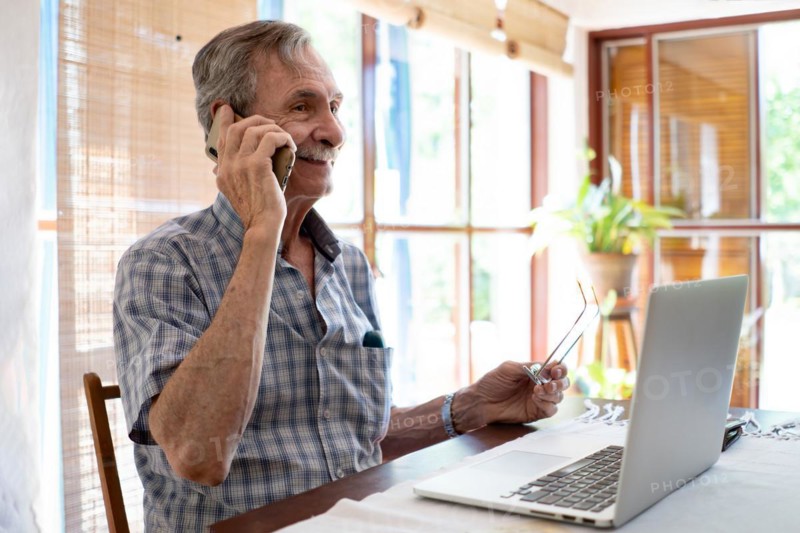 Mature business man smiling and talking on phone in front of laptop
