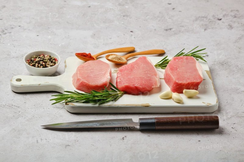 Three uncooked pork cutlets on white cutting board