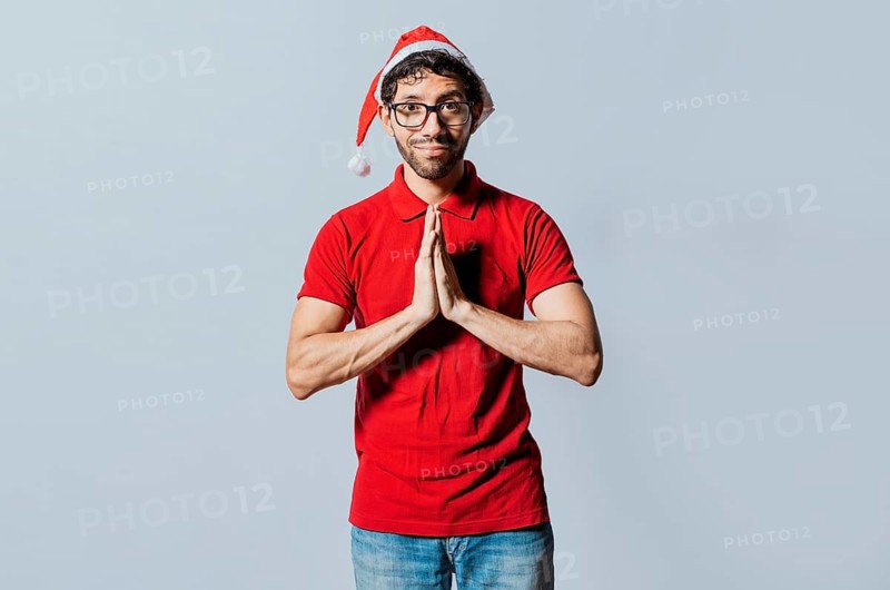 Man in christmas hat with hands together making a wish isolated. Guy with hands together making a christmas wish