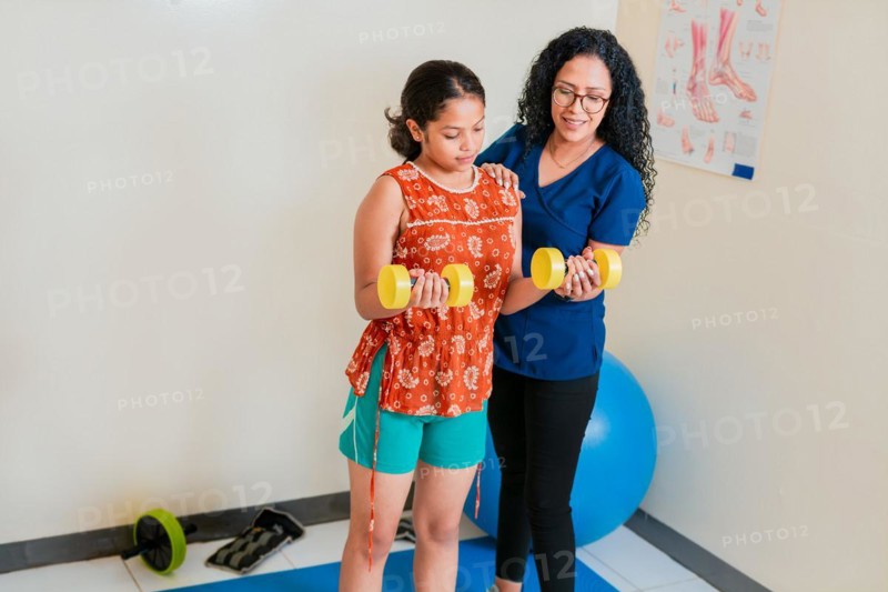 Physiotherapist assisting female patient with dumbbells on rehab ball. Rehabilitation physiotherapy with dumbbells