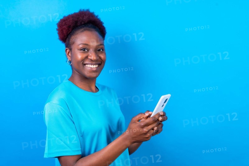 Young african american woman isolated on a blue background smiling with the mobile phone