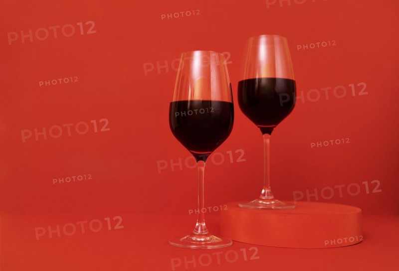 Two glasses of wine on the podium. Red bright background. Minimalism. Close up. Copy space. Valentines Day concept. Mockup for holidays design