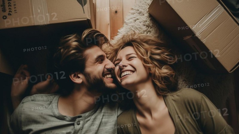 Happy young adult couple laying on the floor of their new home with moving boxes surrounding them
