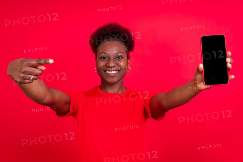 Young african american woman isolated on a red background with mobile pointing gesture