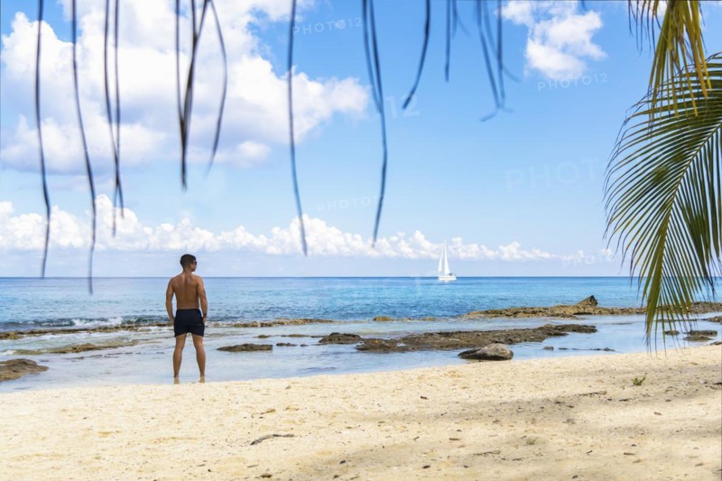 Handsome young man in barefoot swimsuit on the sandy shore