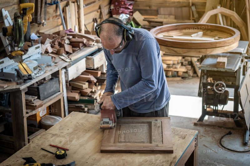 Carpenter sanding a wood with an orbital sander in a workshop