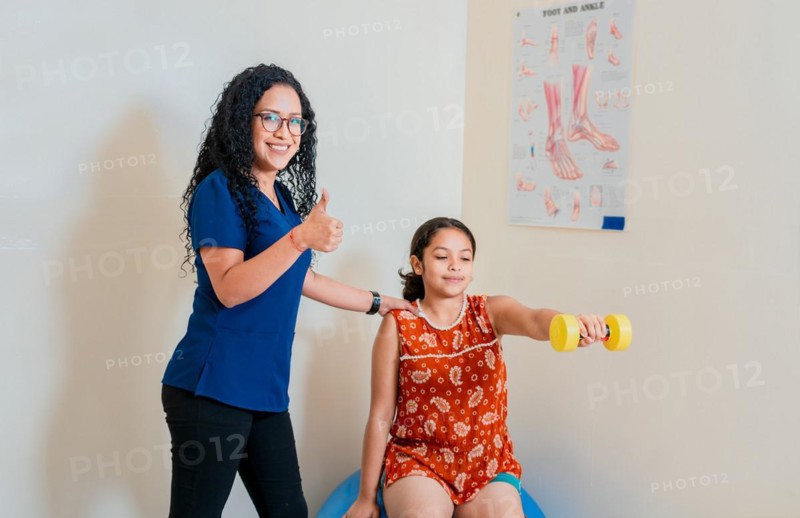 Professional physiotherapist showing thumb up while helping patient with rehabilitation dumbbells. Rehabilitation physiotherapy to patient with dumbbells