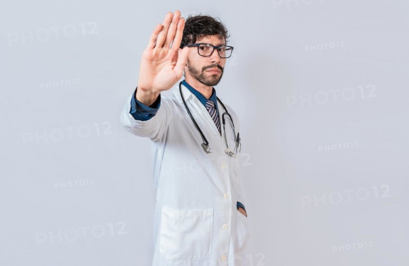 Serious doctor making stop gesture on isolated background
