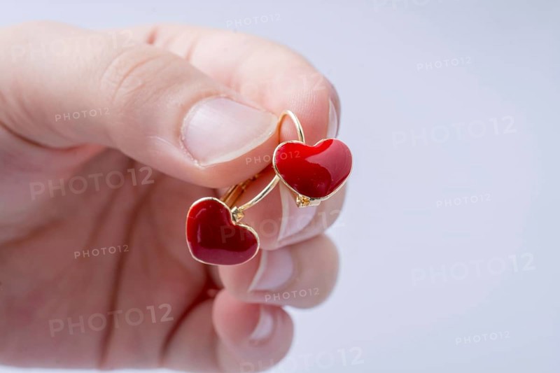 Red color heart shape earring in hand on white