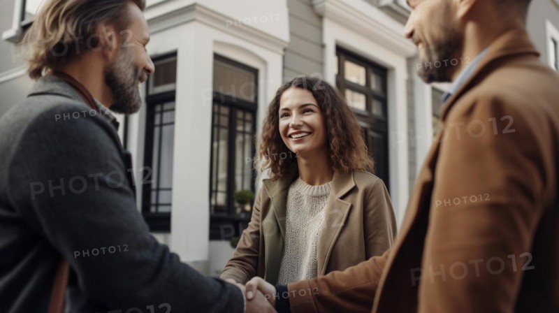 Young adult couple shaking hands with their real estate agent in front of A new house