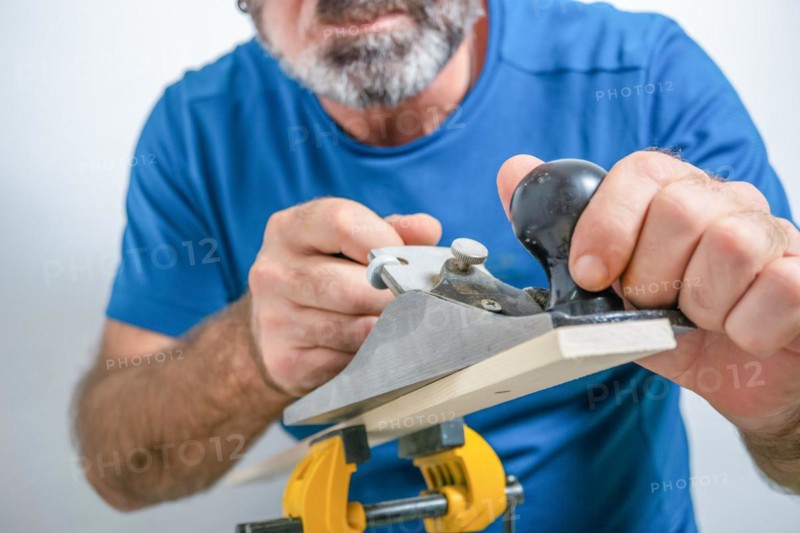 Front view of a bearded male carpenter planing wood with a hand planer isolated on white background
