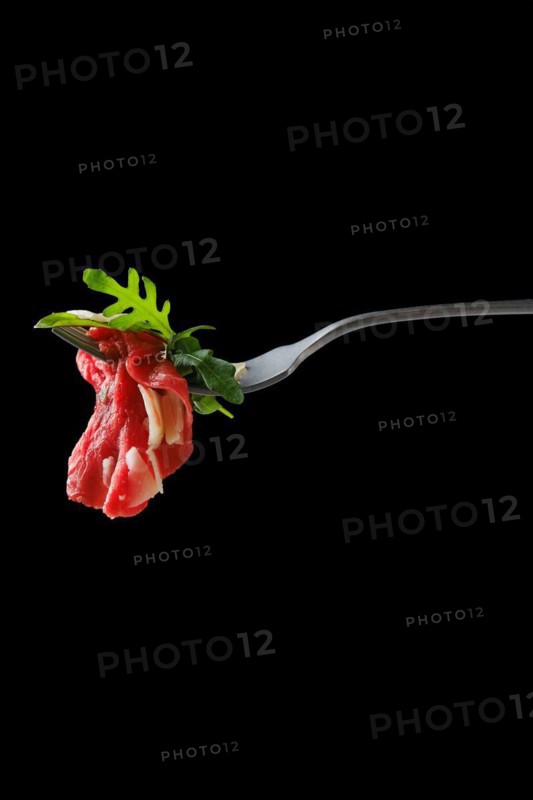 Slice of marbled beef carpaccio on fork over black background