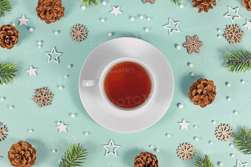 Cup with red tea surrounded by seasonal winter decoration on mint green background