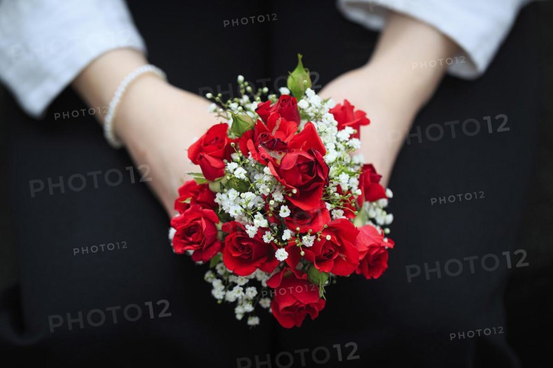 Two hands hold a small bouquet of red roses