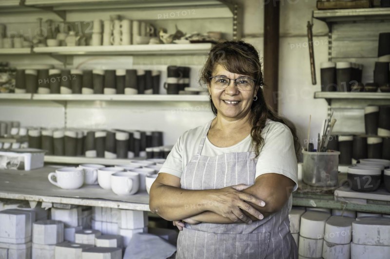 Adult woman potter with glasses and work apron smiling and looking at camera in her studio