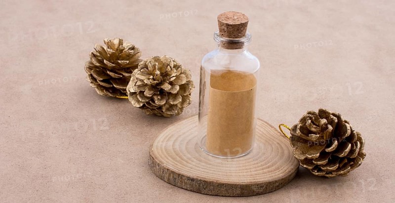 Pine cones and a bottle on a piece of cut wood on a light brown background