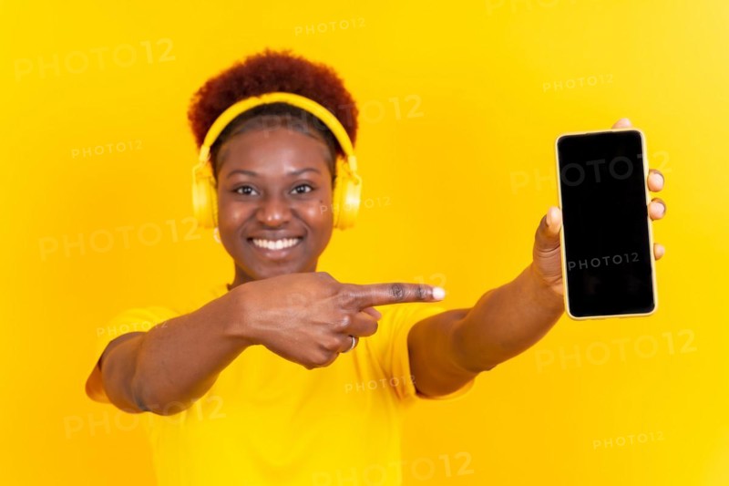 Young african american woman isolated on a yellow background with mobile pointing gesture