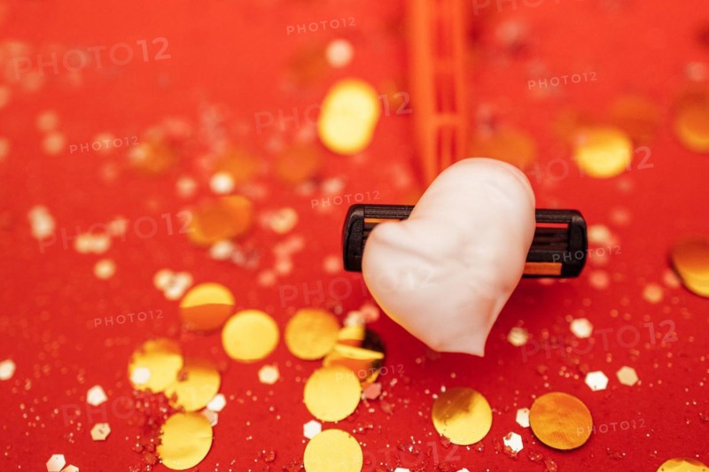 Razor with heart shaped shaving foam. Bright red background with silver glitters and gold round confetti. Copy spase. Bodycare and skincare concept. Close up