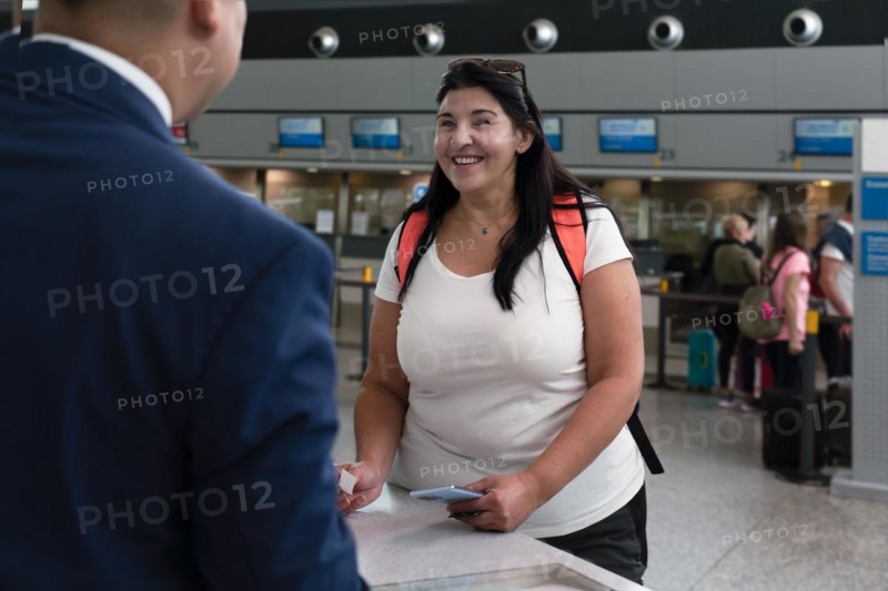 Adult woman smile talking to staff at reception in airport. Woman as a passenger at check in counter
