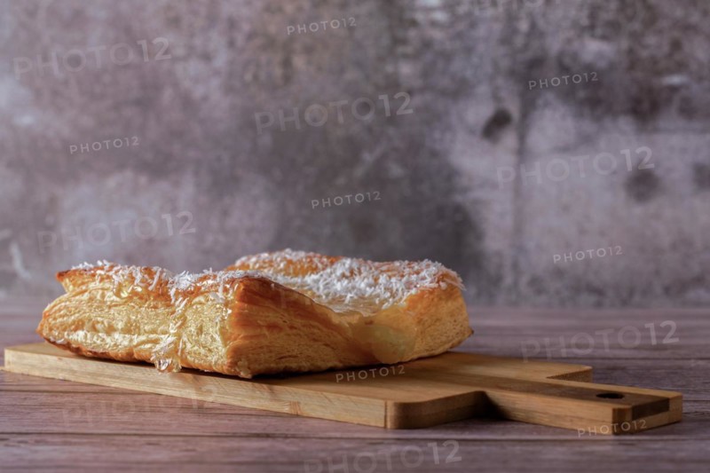 Close-up of an apple tart with shredded coconut on a wooden board with gray background and copy space