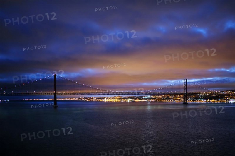 View of 25 de Abril Bridge famous tourist landmark of Lisbon connecting Lisboa and Almada on Setubal Peninsula over Tagus river in the evening twilight. Lisbon