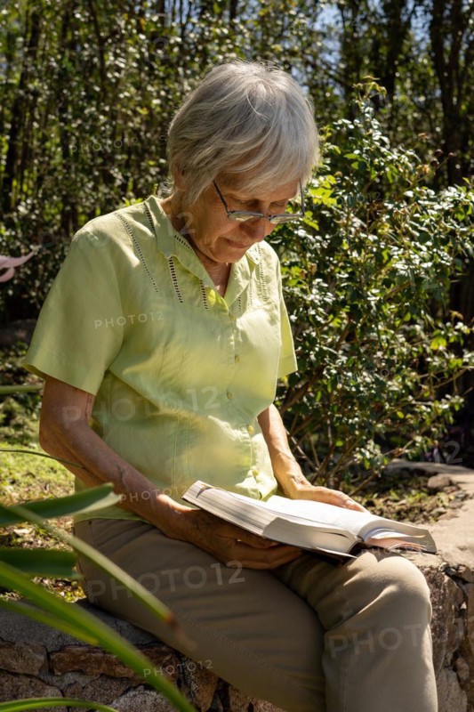 Elegant mature woman reading a book in a park. Vertical portrait