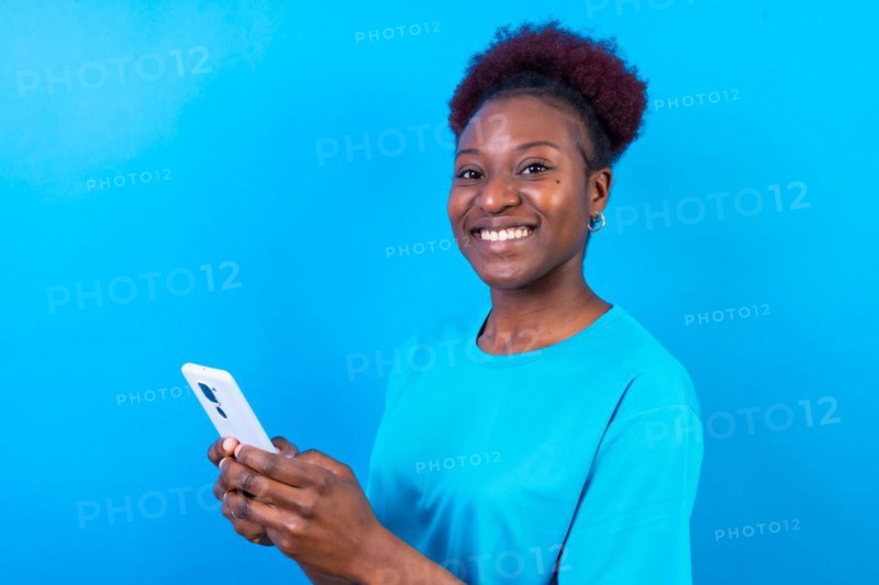 Young african american woman isolated on a blue background smiling with the mobile phone