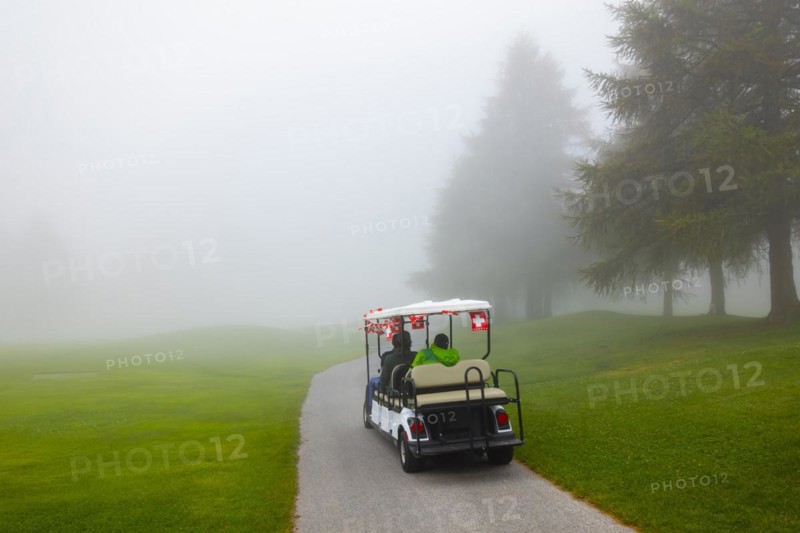 Golf cart with swiss flag on golf course with fog and trees in Crans Montana in Valais