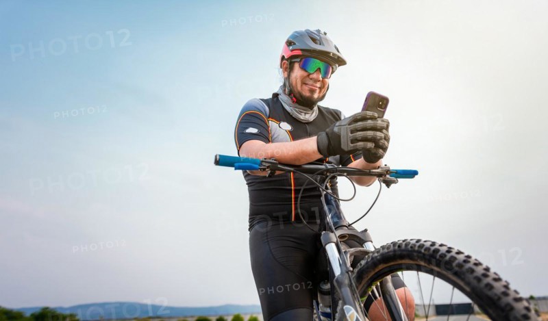 Male cyclist with helmet using cell phone. Cyclist on his bike texting with phone outdoors. cyclist man with helmet and glasses texting on cell phone outdoors