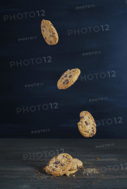 Chocolate cookies falling in a row on a wooden table with dark background and copy space