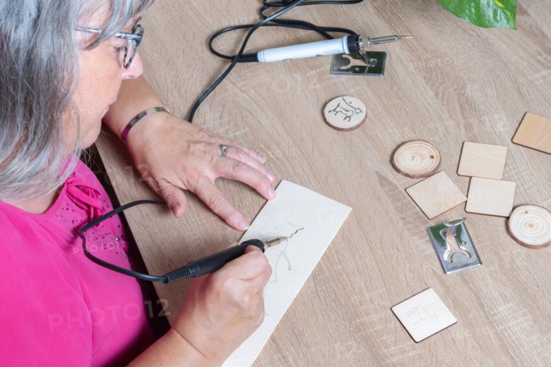 Top view of a woman burning a wooden board with a pyrographer