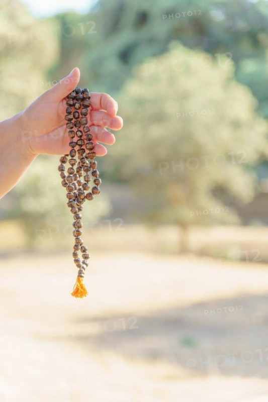 Woman's hands holding a hindu japa mala illuminated by sun in meditation in the countryside at sunset