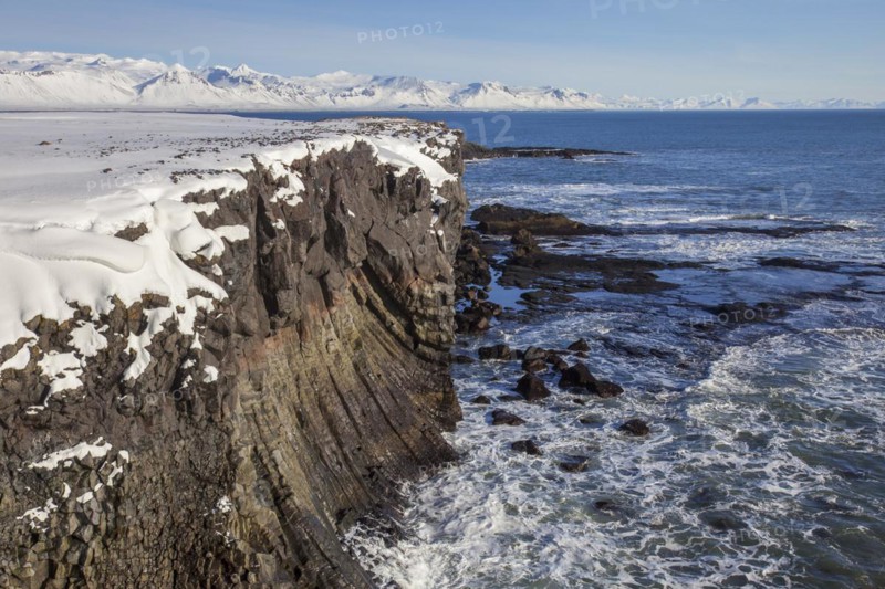 Basalt cliff in the snow in winter along the coast near Arnarstapi