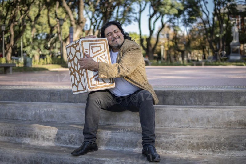 Hispanic musician sitting in a park hugging his flamenco box