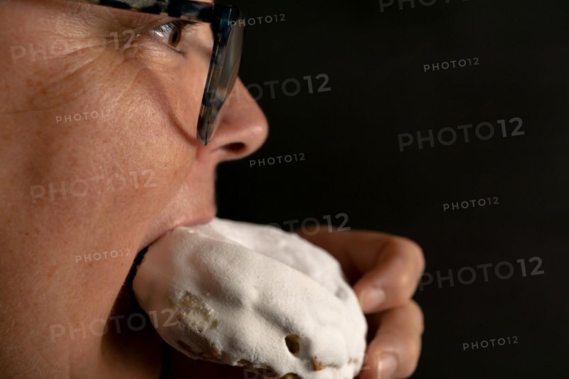 Woman in profile with glasses taking a bite of a glazed sugar doughnut with black background and copy space