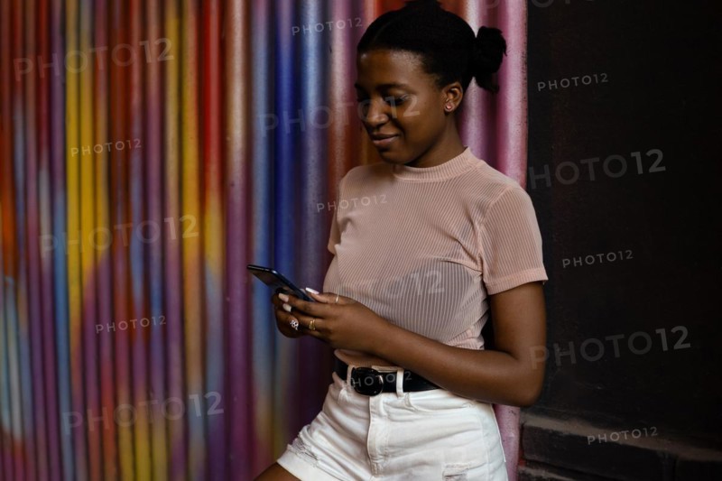 Happy black woman using smart phone and smiling on colorful background