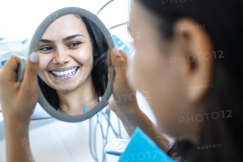 Reflection of a beautiful woman looking in the mirror at the dentist's office. Concept of whitening